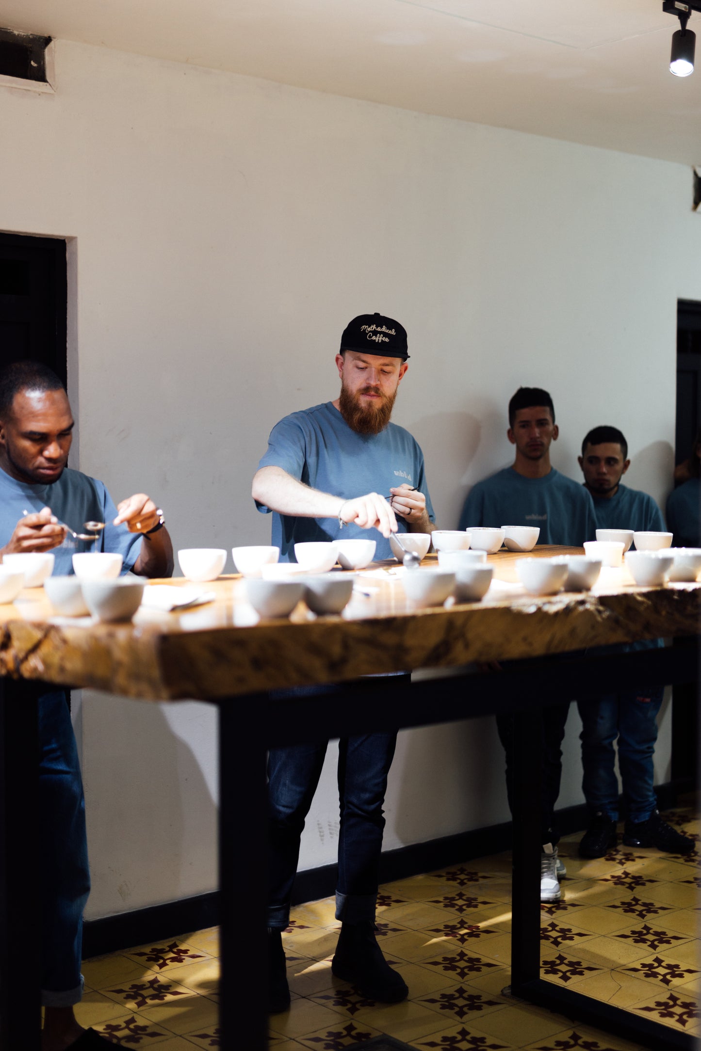 Group of people around a table with small coffee cups, in a specialty coffee tasting or evaluation setting.