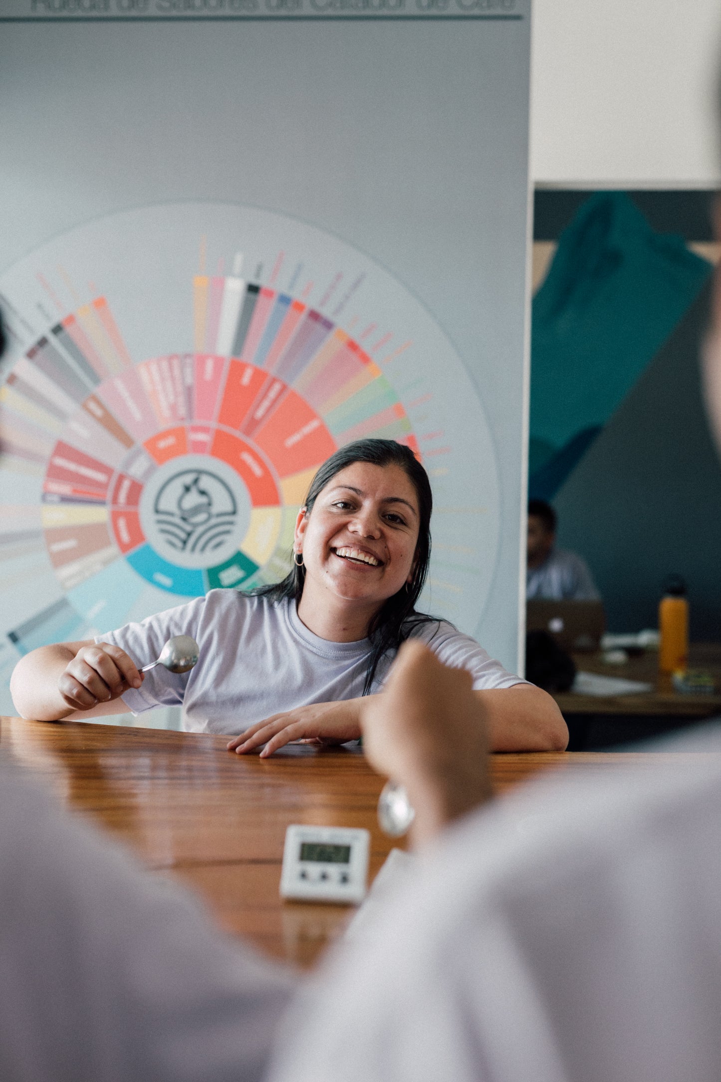 Woman sitting at a table with a colorful wheel of specialty coffee notes poster in the background
