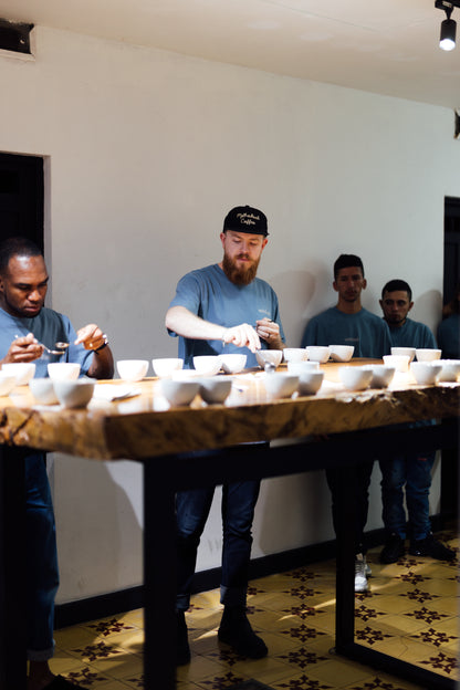 Group of people around a table with small coffee cups, in a specialty coffee tasting or evaluation setting.