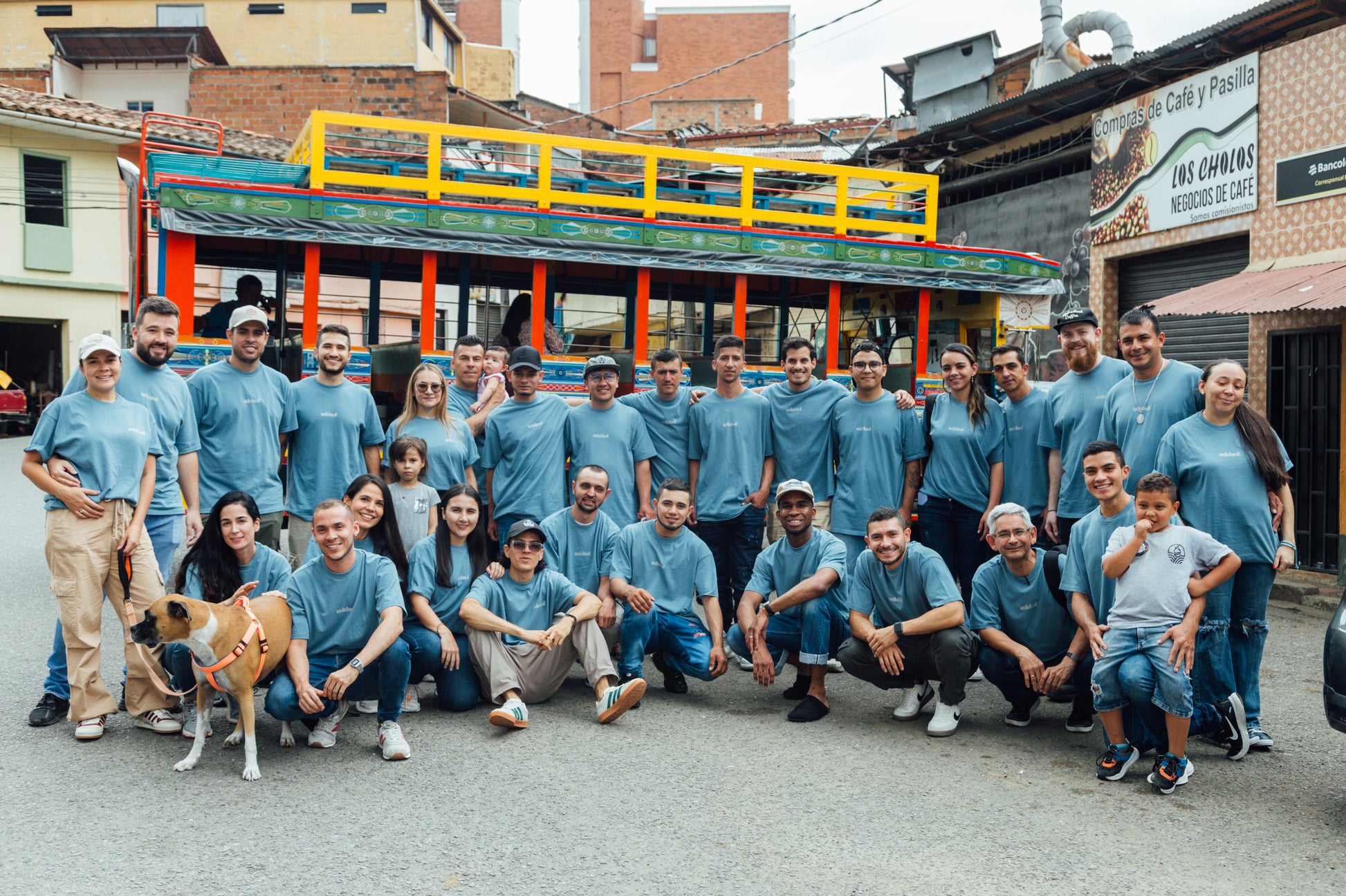 Group of people in matching blue unblended shirts posing in front of a colorful bus.