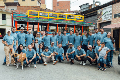 Group of people in matching blue unblended shirts posing in front of a colorful bus.
