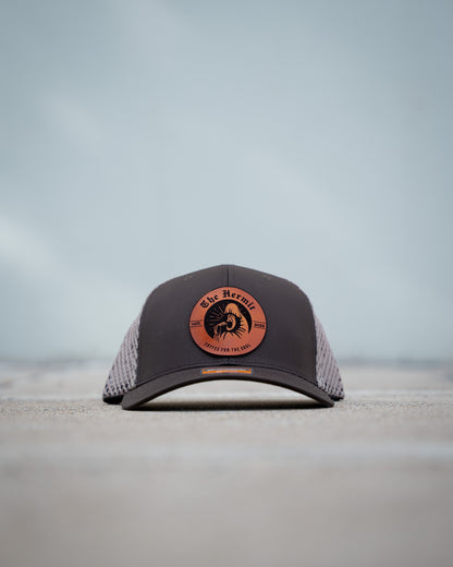 Black and brown The Hermit Specialty Coffee cap with a logo on a light gray background